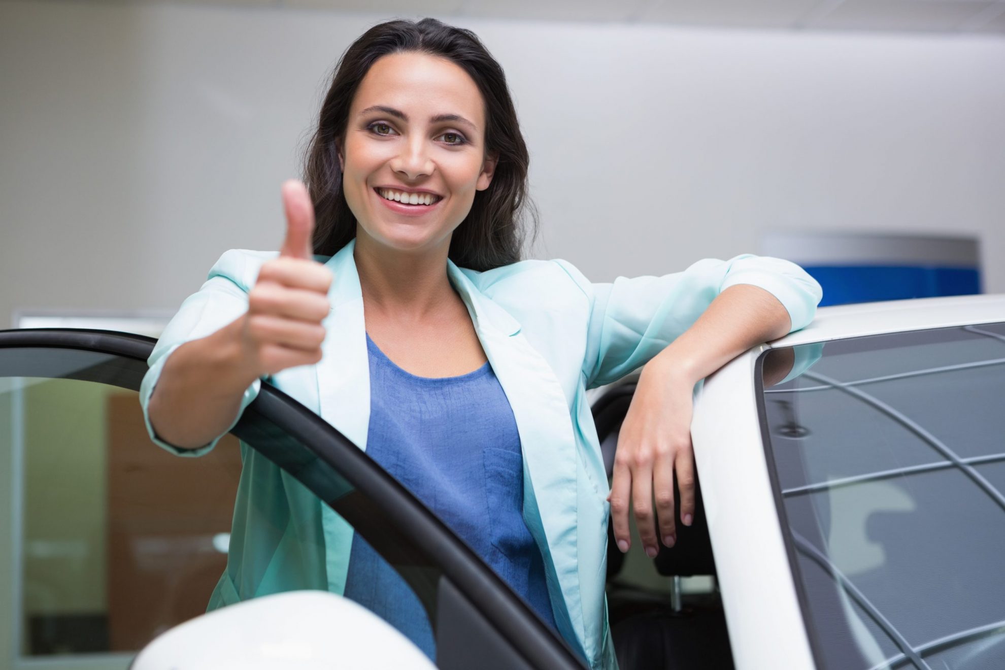 Photo of smiling woman giving the thumbs up leaning on a car illustrates blog: "Looking for Low-Cost Auto Insurance in Texas? Use These Tips"