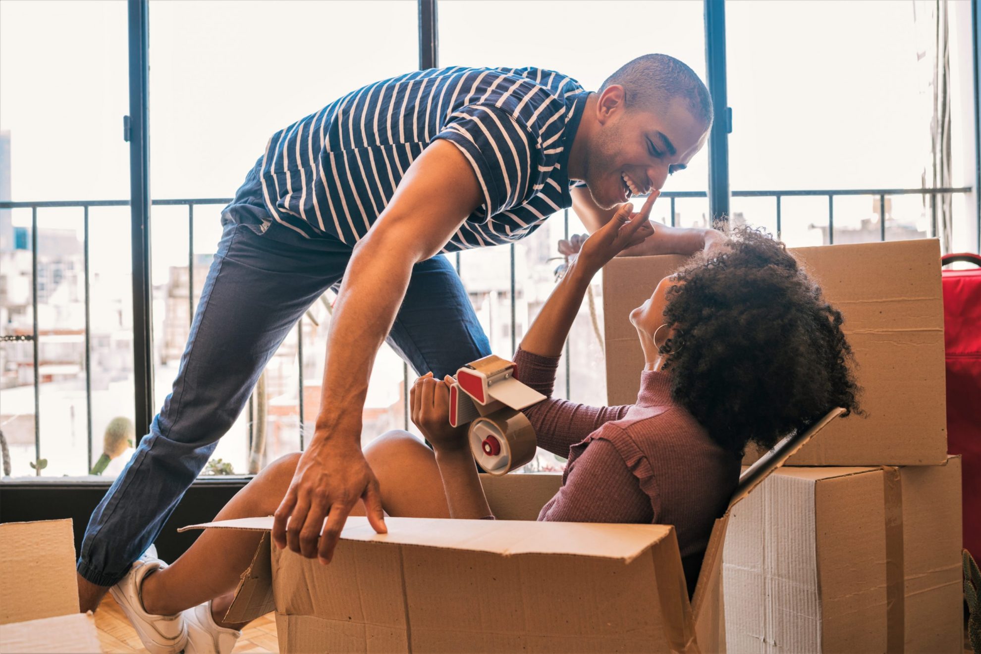 Photo that shows a woman sitting in a cardboard box with a man in leaning down toward her illustrates blog: "Renters Insurance: 4 Things You Need to Know"
