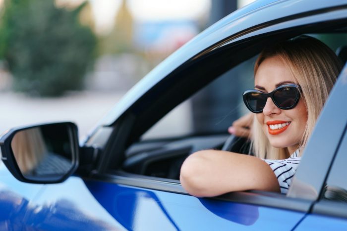 Photo of woman in car wearing sunglasses illustrates blog: "Auto Insurance: Actual Cash Value vs Replacement Cost"